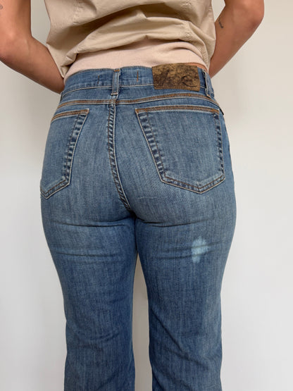 Person wearing blue jeans with a beige shirt against a plain background