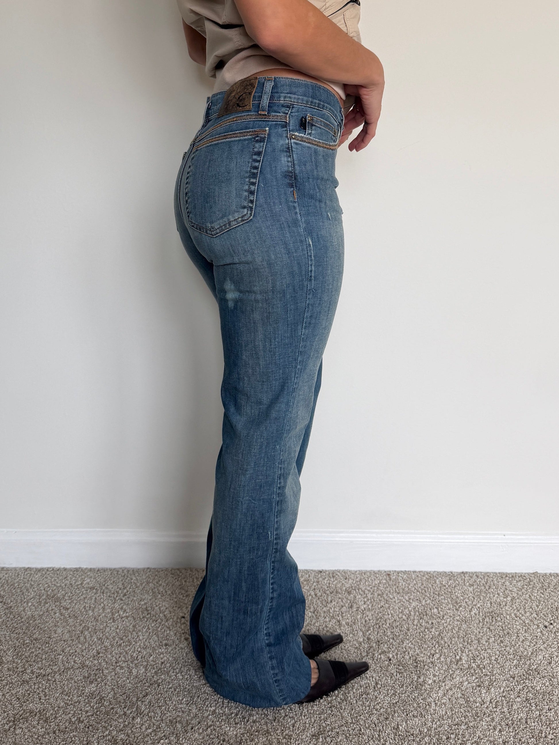 Person wearing blue jeans standing against a plain white wall.