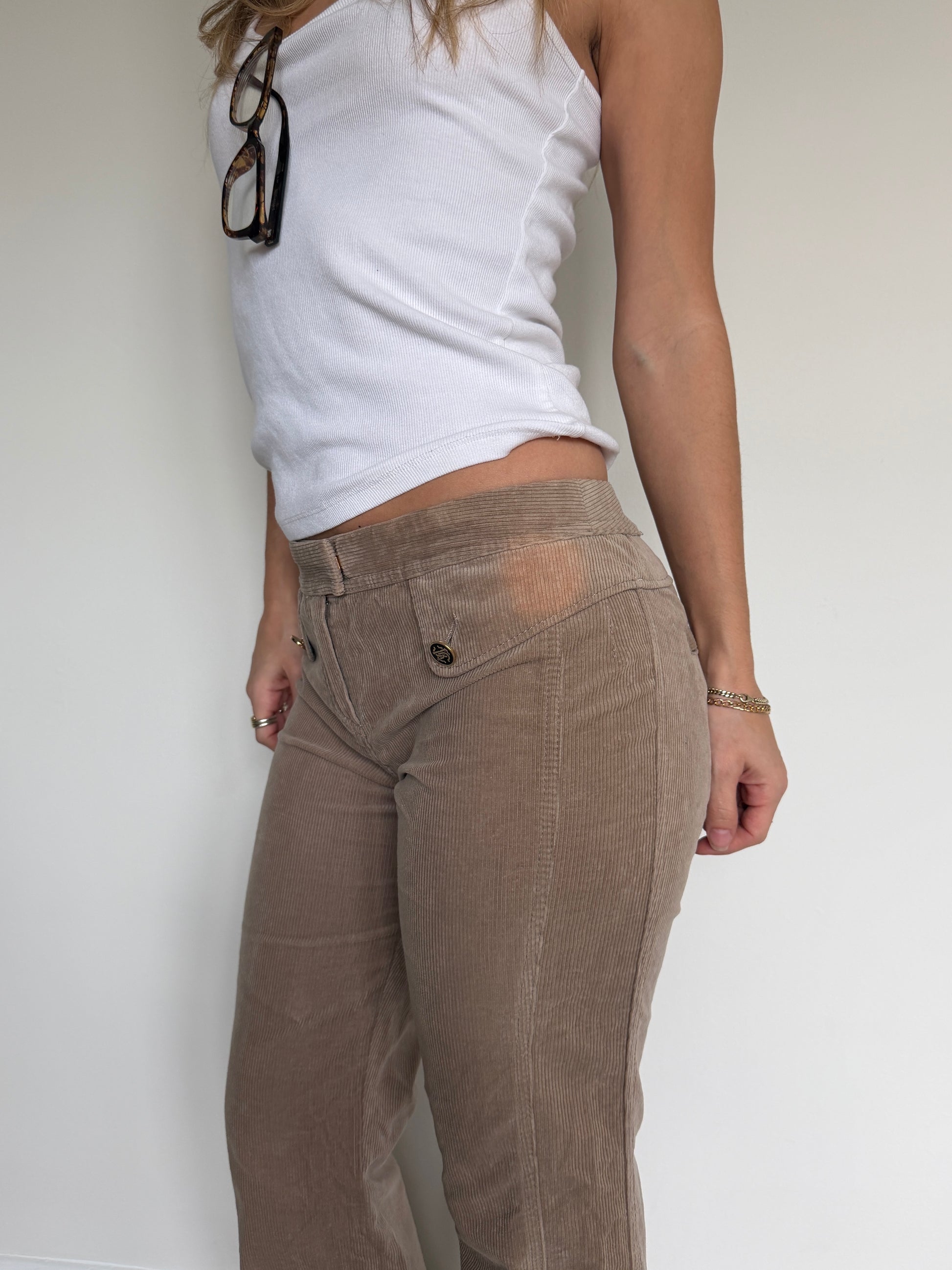 Person wearing a white top and brown pants against a plain background
