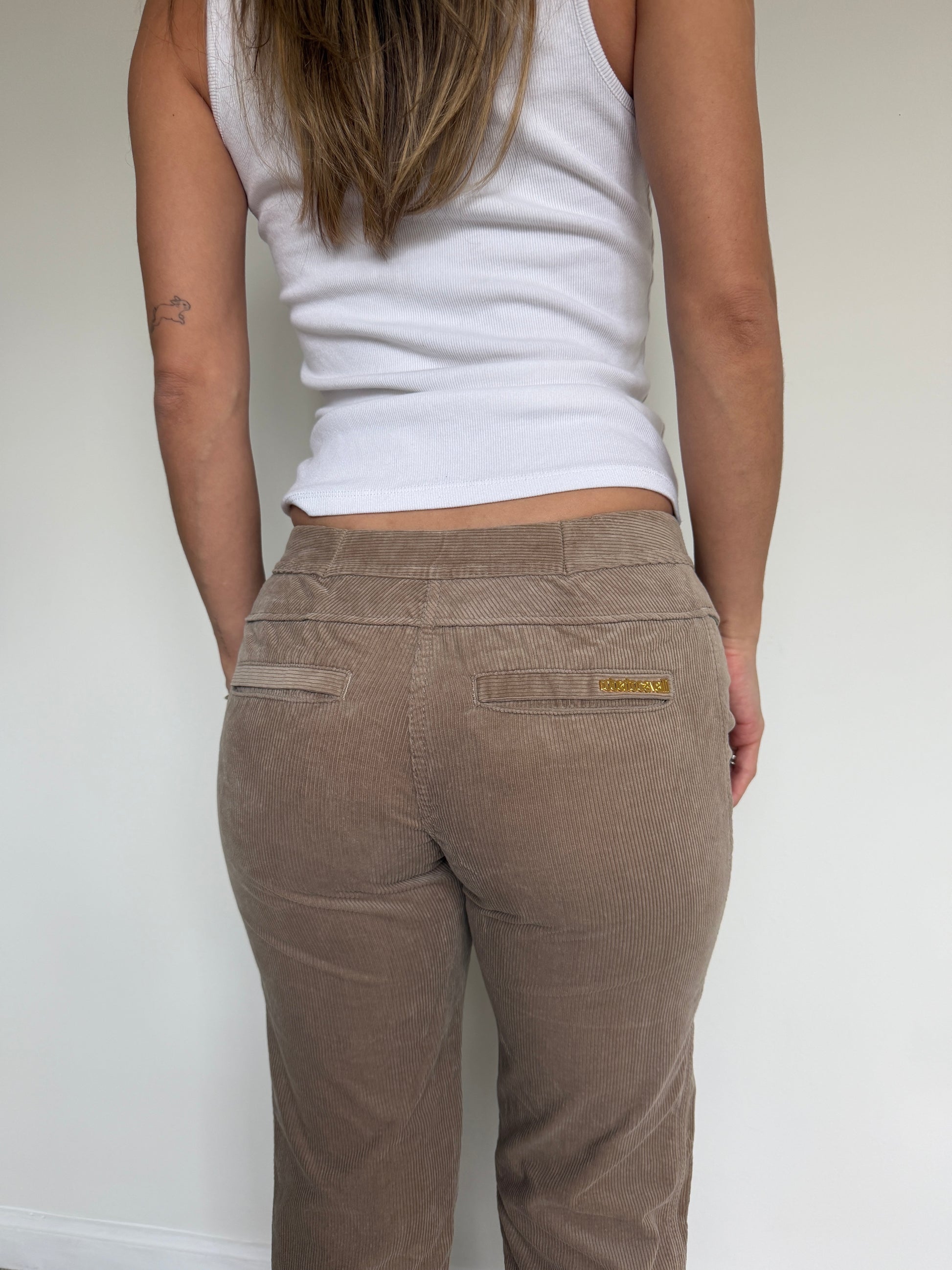 Person wearing a white tank top and brown pants against a plain background