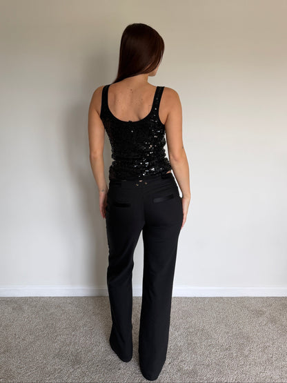 Person wearing a black sequin top and black pants against a plain wall.