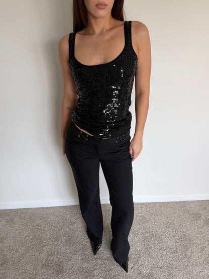 Person wearing a black sequin tank top and black pants against a plain background