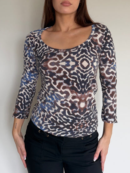 Woman wearing a patterned long-sleeve top against a plain background