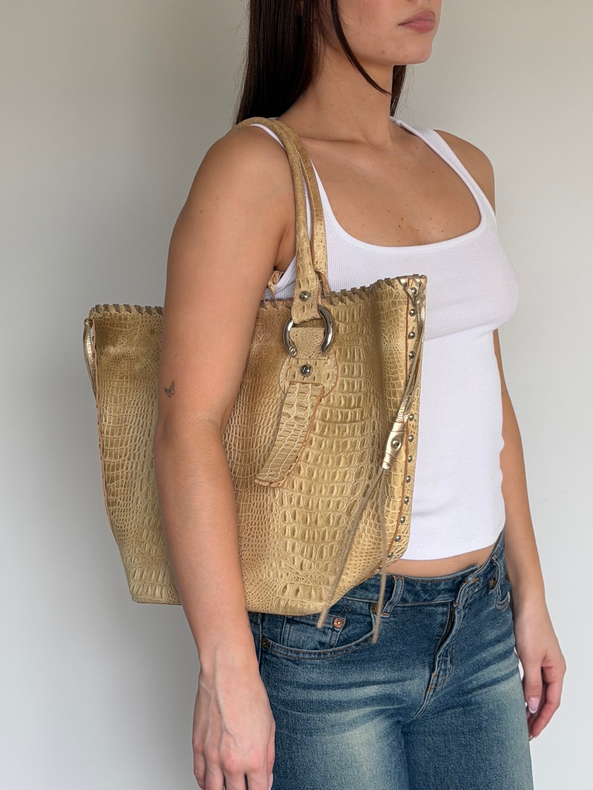 Woman carrying a textured beige handbag against a plain background