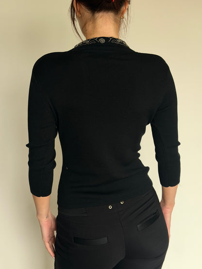 Person wearing a black long-sleeve top and black pants against a beige background