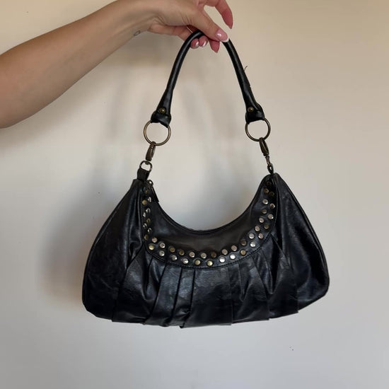 Black handbag with studs on a beige wall