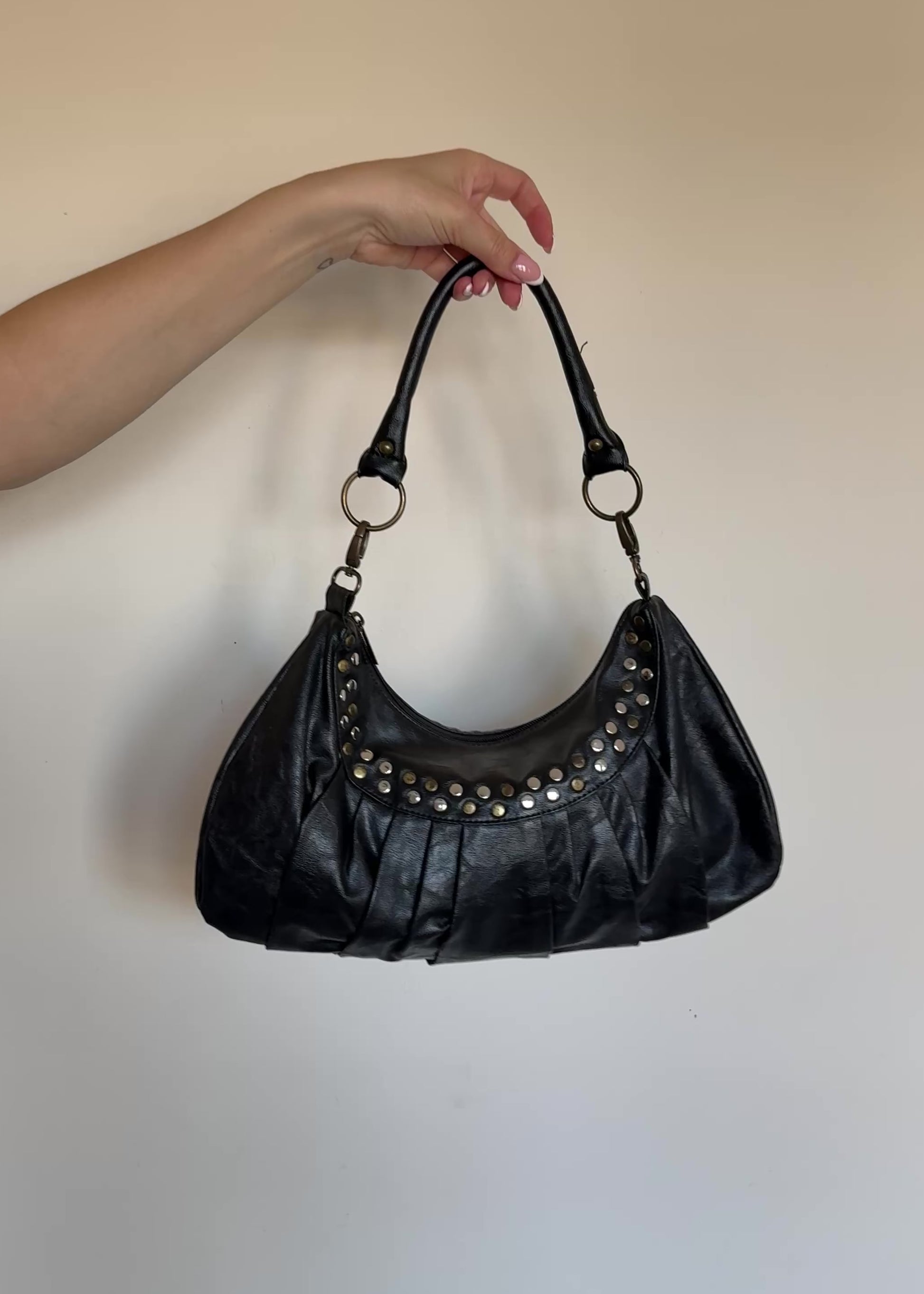 Black handbag with studs on a beige wall
