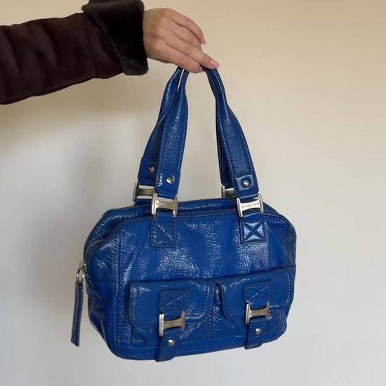 Blue handbag with silver hardware on a white wall