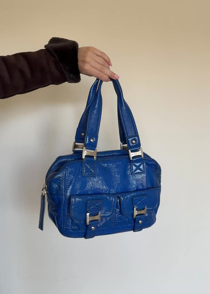Blue handbag with silver hardware on a white wall