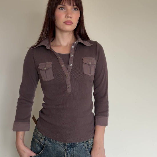 Woman wearing a brown long-sleeve shirt with pocket details against a plain background