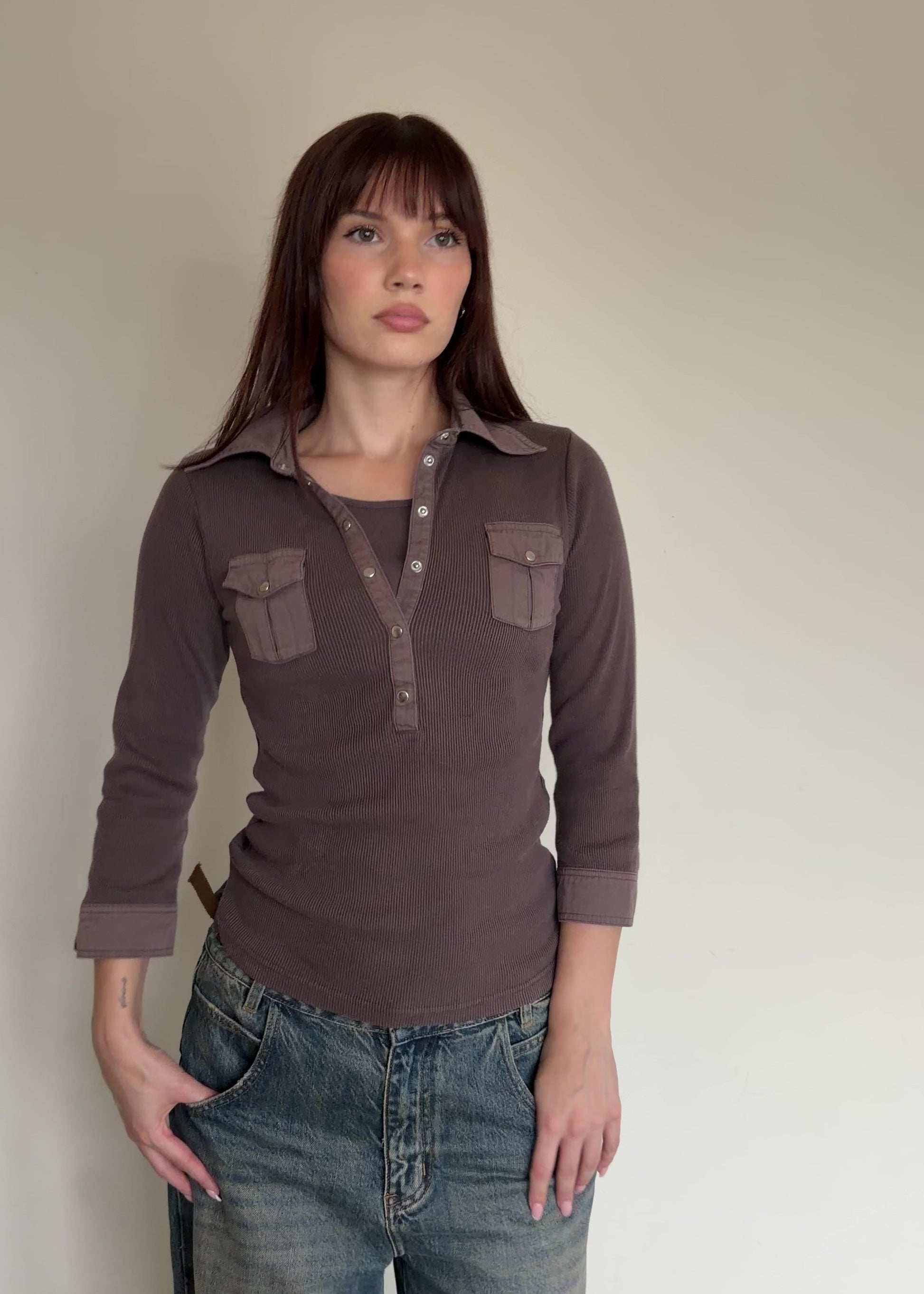 Woman wearing a brown long-sleeve shirt with pocket details against a plain background
