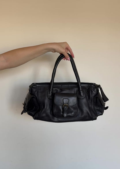Black leather bag held by a hand against a plain background